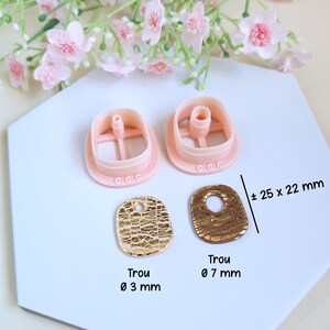 Puede incluir: Un conjunto de cortadores de arcilla polim&eacute;rica rosa y dos colgantes dorados texturizados. Los colgantes miden aproximadamente 25 x 22 mm. Un colgante tiene un agujero de 3 mm, el otro de 7 mm. Flores rosas en el fondo.