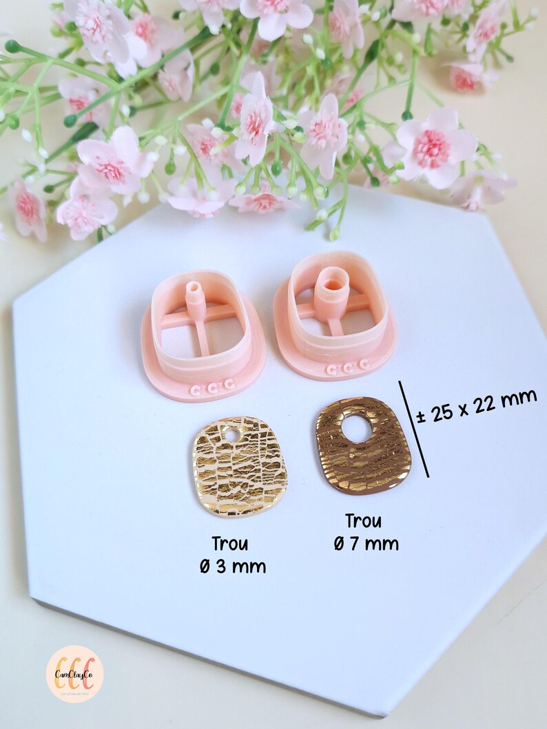 Puede incluir: Un conjunto de cortadores de arcilla polim&eacute;rica rosa y dos colgantes dorados texturizados. Los colgantes miden aproximadamente 25 x 22 mm. Un colgante tiene un agujero de 3 mm, el otro de 7 mm. Flores rosas en el fondo.