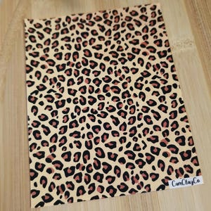 May include: A sheet of beige vinyl with a leopard print pattern in black and brown. The vinyl sheet has the text "CamClayCo" printed in white in the bottom right corner.