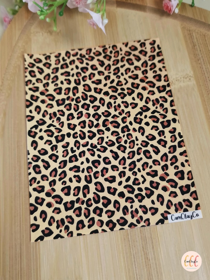May include: A sheet of beige vinyl with a leopard print pattern in black and brown. The vinyl sheet has the text "CamClayCo" printed in white in the bottom right corner.