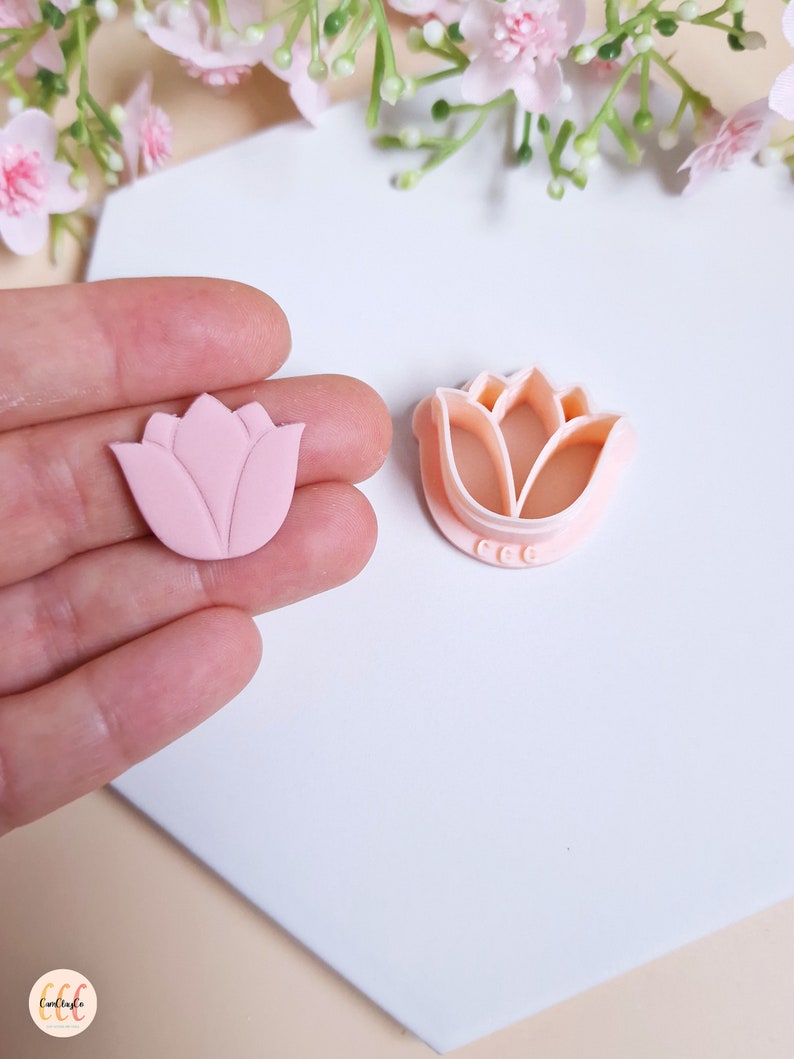 Op de afbeelding: Een roze polymer clay tulpenbloem en een plastic tulpenkoekjesvormpje. Het koekjesvormpje heeft de letters "CCC" op de onderkant.