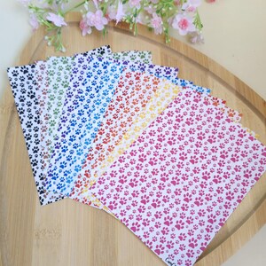 Puede incluir: Una colección de hojas rectangulares con un patrón repetitivo de pequeñas huellas de patas en varios colores, incluyendo negro, verde, azul, naranja, amarillo y rosa. Cada hoja muestra el texto CamClayCo en la esquina inferior.