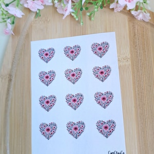 Könnte beinhalten: Ein Bogen Aufkleber mit floralen Herzmotiven. Jedes Herz besteht aus kleinen grünen Blättern und rosa Blüten, mit einer größeren rosa Blüte in der Mitte. Die Aufkleber befinden sich auf weißem Hintergrund, mit dem Markennamen "CamClayCo" sichtbar.