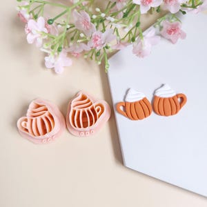 Peut inclure: Un ensemble de cinq boucles d'oreilles en pâte polymère sur le thème de l'automne. Deux boucles d'oreilles sont en forme de tasse à café avec un tourbillon blanc sur le dessus et un glaçage brun. Les trois autres boucles d'oreilles sont en forme de tasse à café avec un tourbillon blanc sur le dessus et un glaçage rose.