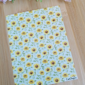 Peut inclure: Une feuille de simili cuir bleu clair avec un motif répétitif de tournesols jaunes. Le texte "CamClayCo" est imprimé en noir dans le coin inférieur droit.