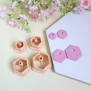 Può includere: Quattro tagliapasta esagonali color pesca con espulsori centrali e quattro forme esagonali piatte in argilla rosa. I tagliapasta presentano il testo in rilievo CamClayCo e gli indicatori di dimensione 15, 20, 25 e 30.