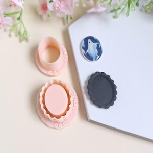 Op de afbeelding: Een set van drie roze plastic koekjesvormen, een ronde, een ovale en een met een spookontwerp. De vormen liggen op een wit oppervlak met een witte achtergrond.