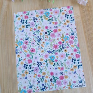 Puede incluir: Una hoja de papel blanca con un patrón floral con flores rosas, azules, amarillas y verdes. El texto "CamClayCo" está impreso en la esquina inferior derecha.
