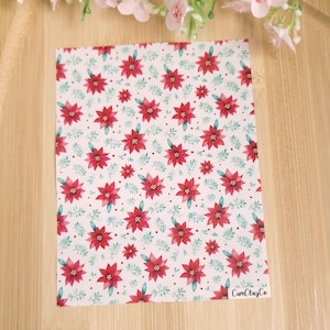 Peut inclure: Fond blanc avec un motif répété de fleurs de poinsettia rouges, de feuilles vertes et de petits points blancs. Le texte "CamClayCo" est dans le coin inférieur droit.