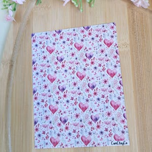 Könnte beinhalten: Eine rechteckige Karte mit einem Blumen- und Herzmuster. Das Design zeigt rosa und lila Herzen und Blumen auf weißem Hintergrund. Der Text "CamClayCo" ist unten rechts aufgedruckt.