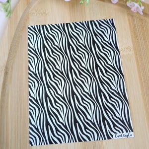 Op de afbeelding: Zwart-wit zebraprint patroonpapier. Het papier heeft een glanzende afwerking en is perfect voor knutselprojecten. Het papier is gelabeld met "CamClayCo."