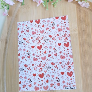 Peut inclure: Une carte rectangulaire avec un fond blanc, ornée d'un motif de cœurs, de fleurs et de feuilles rouges. La carte est décorée d'éléments floraux roses et rouges. Le texte "CamClayCo" est visible dans le coin inférieur droit.