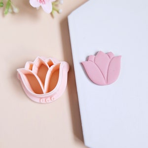 Op de afbeelding: Een roze plastic tulpenkoekjesvormpje en een roze fondanttulip. De koekjesvormpje heeft een gedetailleerd ontwerp en de fondanttulip is licht verhoogd.