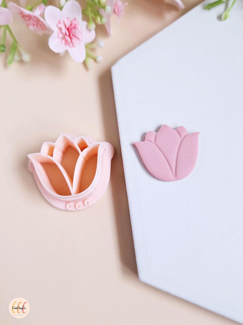 Op de afbeelding: Een roze plastic tulpenkoekjesvormpje en een roze fondanttulip. De koekjesvormpje heeft een gedetailleerd ontwerp en de fondanttulip is licht verhoogd.