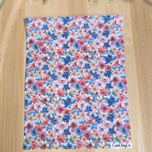 Puede incluir: Una lámina rectangular con un estampado floral con flores rojas, azules y melocotón sobre un fondo blanco. Las flores están densamente empaquetadas, creando un diseño vibrante y colorido. El texto "CamClayCo" es visible en la esquina inferior derecha.