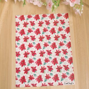 Peut inclure: Fond blanc avec un motif répété de fleurs de poinsettia rouges et de feuilles vertes. Le texte "CamClayCo" est dans le coin inférieur droit.