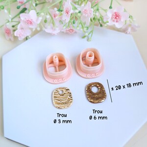 Puede incluir: Dos cortadores de pendientes de pl&aacute;stico rosa y dos piezas en bruto de pendientes de metal texturizado dorado. Las piezas en bruto de los pendientes miden aproximadamente 20 x 18 mm. El texto "Trou" y los di&aacute;metros de los agujeros tambi&eacute;n son visibles.