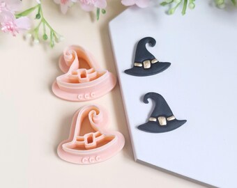 Op de afbeelding: Twee roze plastic heksenhoed koekjesvormen en twee zwarte fondant heksenhoeden met gouden accenten.