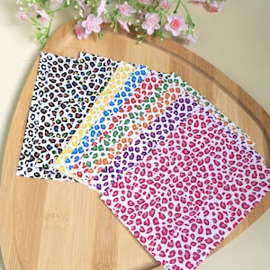 May include: A collection of colorful leopard print sheets arranged on a wooden tray. The sheets feature various colors, including black, white, yellow, blue, red, orange, purple, and pink. The sheets are decorated with a leopard print pattern.