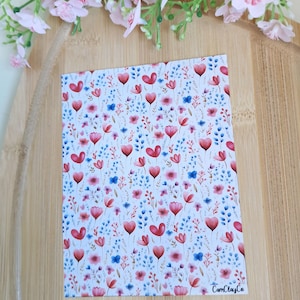 Peut inclure: Une carte rectangulaire avec un motif floral composé de fleurs rouges en forme de cœur, de fleurs roses et bleues, et de feuilles vertes sur fond blanc. Le texte "CamClayCo" est visible en bas à droite.