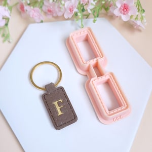 May include: A pink plastic cookie cutter shaped like a pair of glasses, and a brown leather keychain with a gold letter F.