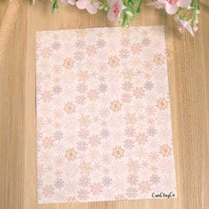Peut inclure: Une feuille de papier blanche avec un motif répétitif de flocons de neige roses, orange et gris. Le papier porte le texte "CamClayCo" dans le coin inférieur droit.