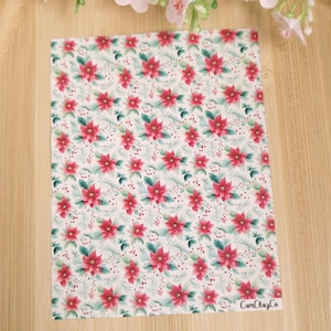 Peut inclure: Tissu blanc avec un motif répété de fleurs de poinsettia rouges, de feuilles vertes et de petites baies rouges. Le tissu porte le texte "CarnClayCo" dans le coin inférieur droit.
