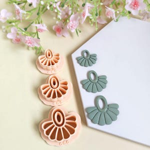 Könnte beinhalten: Drei rosa und drei grüne Polymer Clay Ohrringausstecher in Fächerform. Die Ausstecher sind in verschiedenen Größen. Die rosa Ausstecher befinden sich auf einer hellgelben Oberfläche und die grünen auf einer weißen Oberfläche. Rosa Blumen im Hintergrund.