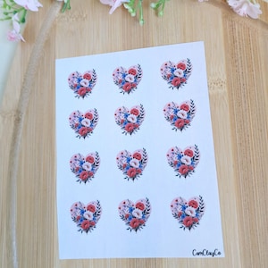 Könnte beinhalten: Ein Bogen Aufkleber mit herzförmigen Blumendesigns. Jedes Herz enthält einen Strauß aus roten, blauen und weißen Blumen, umgeben von grünen Blättern. Die Aufkleber befinden sich auf weißem Hintergrund, mit dem CamClayCo-Logo.