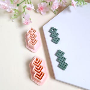 May include: Two pink polymer clay cutters and two sets of green polymer clay earrings. The cutters have a layered chevron design. The earrings are a dark green with a speckled pattern and a similar chevron design.