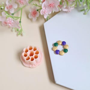 May include: Two pink silicone moulds for making honeycomb-shaped sweets. One mould is a circle with eight honeycomb shapes. The other mould is a ring with eight round shapes. The ring mould has purple and green dots.