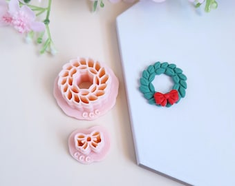 Könnte beinhalten: Drei rosafarbene Ausstecher aus Polymer Clay, einer in Form eines Kranzes mit einer roten Schleife, einer in Form einer Schleife und einer in Form eines Kranzes mit einem detaillierten Design.