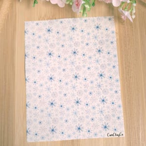 Peut inclure: Une feuille de papier rectangulaire avec un fond blanc et un motif de flocons de neige bleus. Le papier porte le texte "CamClayCo" dans le coin inférieur droit. Des fleurs roses sont en haut de l'image.