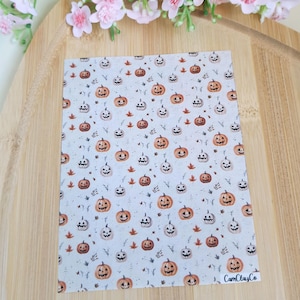 Puede incluir: Una hoja de papel rectangular con un patrón repetido de calabazas naranjas y blancas y hojas marrones sobre un fondo blanco. El papel tiene el texto "CamClayCo" en la esquina inferior derecha.