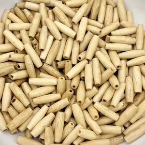 May include: A white bowl filled with natural wood beads. The beads are light brown and have a smooth, polished finish.