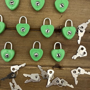 May include: A collection of 10 green heart-shaped padlocks with silver keys. The padlocks are arranged in a grid pattern on a wooden surface.