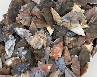 Puede incluir: Una gran colección de puntas de flecha hechas de varios tipos de piedra, incluyendo ágata, jaspe y sílex. Las puntas de flecha son de diversas formas y tamaños, y todas son de tonos marrones, grises y rojos.