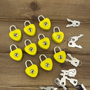 May include: A set of ten yellow heart-shaped combination locks with matching keys. The locks and keys are arranged on a wooden surface.