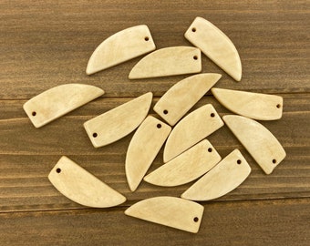 May include: A group of 12 natural wood, light brown, teardrop-shaped pendants with a hole at the top. The pendants are scattered on a wooden surface.