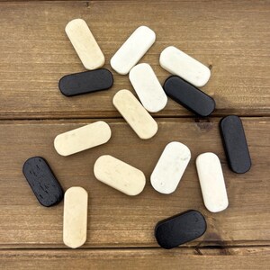 May include: A collection of small, rectangular wooden plugs in various colors: black, white, and beige. The plugs are arranged on a wooden surface, showcasing their rounded edges and smooth finish. The plugs are likely for furniture or woodworking.