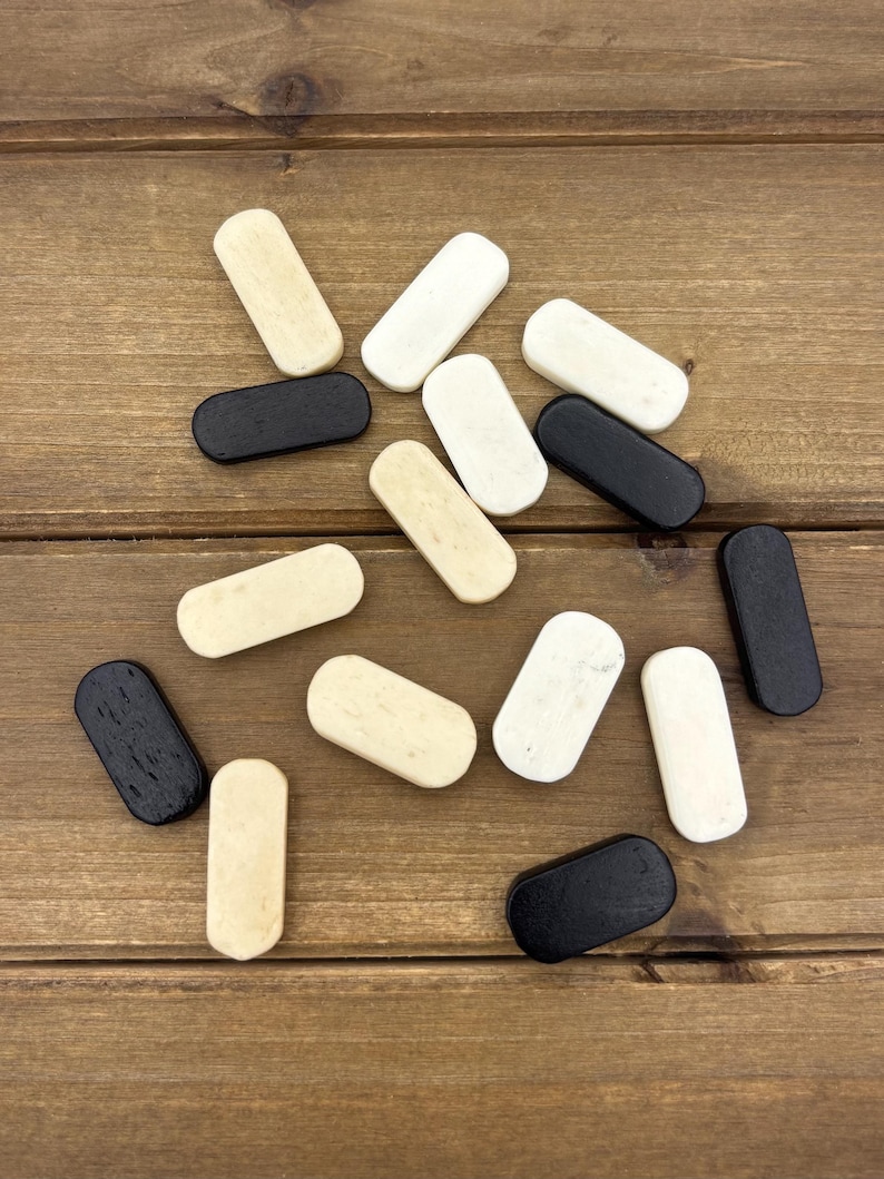 May include: A collection of small, rectangular wooden plugs in various colors: black, white, and beige. The plugs are arranged on a wooden surface, showcasing their rounded edges and smooth finish. The plugs are likely for furniture or woodworking.