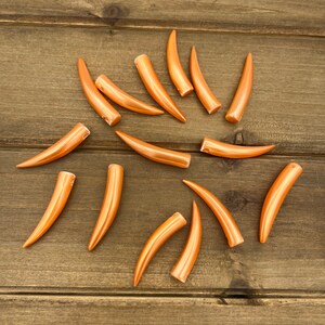 May include: A collection of 14 orange plastic faux tusks, arranged in a circular pattern on a wooden surface.