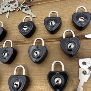 May include: A set of ten black heart-shaped padlocks with silver keys. The padlocks are arranged in a semi-circle on a wooden surface.