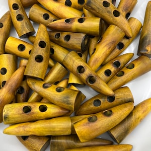 May include: A pile of yellow wooden toggle buttons with two holes each. The buttons are shaped like a long, thin oval with a pointed end.