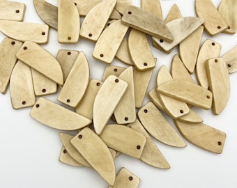 May include: A pile of light brown bone-like pendants in the shape of a crescent moon and a rectangle. The pendants have two holes for stringing.