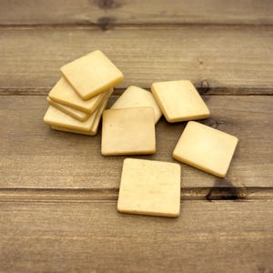 Puede incluir: Una pila de seis azulejos cuadrados de madera de color marr&oacute;n claro sobre una superficie de madera.