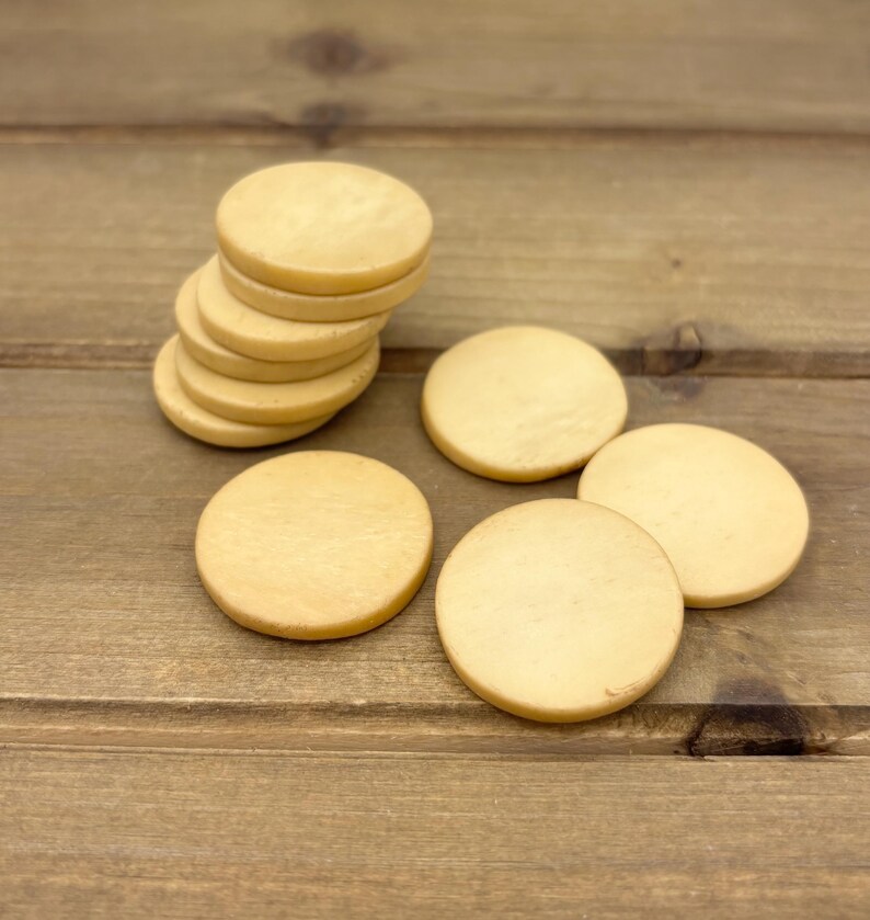 Puede incluir: Una pila de seis posavasos redondos de madera beige. Cuatro posavasos adicionales est&aacute;n esparcidos sobre una superficie de madera.