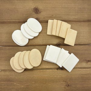 May include: A collection of wooden craft shapes including four white oval pieces, four light tan rectangular pieces, four light tan oval pieces, and four white rectangular pieces arranged in four distinct groups on a flat surface.