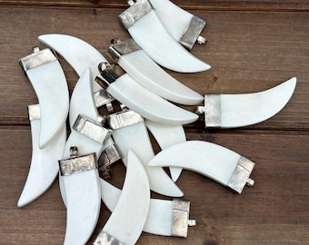 May include: A pile of white, crescent-shaped pendants with silver metal accents. The pendants are arranged on a brown wooden surface.