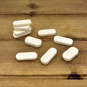 May include: A collection of small, rectangular, off-white objects, possibly erasers or decorative pieces, are scattered on a wooden surface. Some are stacked, while others are arranged individually. The objects have rounded edges and a smooth texture.